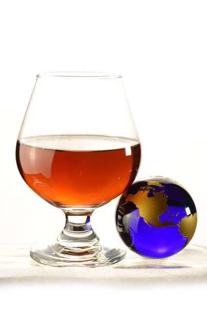 A globe and glass of Cognac over a white background. - Foto, afbeelding