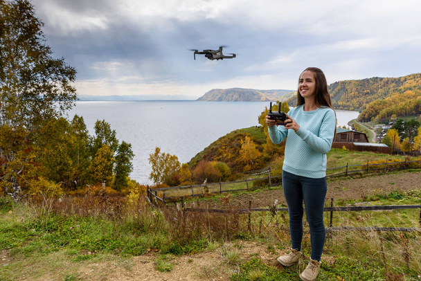 Schöne junge Frau, die Spaß mit einer Mini-Drohne im Freien hat. Das Mädchen steht vor dem herbstlichen Waldhintergrund - Foto, Bild