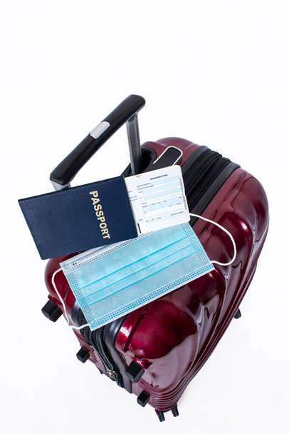 白い背景に隔離された旅行スーツケース、パスポート、搭乗券、医療マスク。Covid-19パンデミックの間の移動制限または禁止の概念とコロナウイルスに対する隔離。垂直方向. - 写真・画像