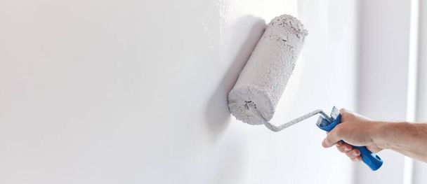 Mężczyzna ręka malowanie ściany z rolki farby. Malowanie mieszkania, remont z białym farbą kolor - Zdjęcie, obraz