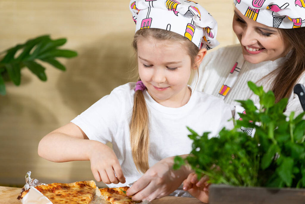Decorating by mother and her five-year-old daughter freshly baked pizza with green leaves of various herbs. Mom and daughter moments together in the home kitchen. - Foto, imagen