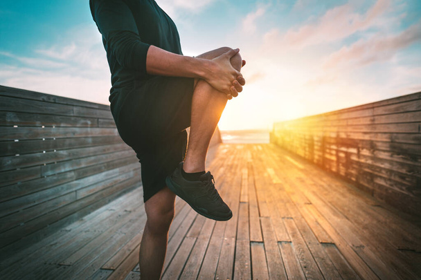 Фітнес-людина розігріває і розтягує ноги перед тренуванням на свіжому повітрі на заході або сході сонця. Спорт і здоровий спосіб життя
 - Фото, зображення