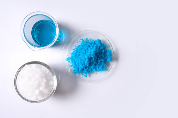 Epäorgaaninen kemikaali valkoisella laboratoriopöydällä. Kupari (II) sulfaatti, mikrokiteinen vaha, alkoholi. Kosmetiikan ja hygieniatuotteiden kemiallinen ainesosa. Ylhäältä - Valokuva, kuva