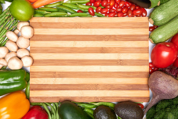 Biologische gemengde groenten bovenaanzicht met een bamboe snijplank met reclame kopieerruimte. Schoon eetconcept, veganistisch of vegetarisch. - Foto, afbeelding