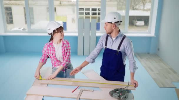 kobieta i mężczyzna wbudowane twarde kapelusze miara laminat z miarą taśmy do renowacji podłogi w nowym mieszkaniu - Materiał filmowy, wideo