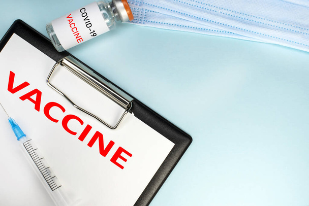 Concepto médico. Una vacuna contra el coronavirus. La ampolla se encuentra entre una máscara médica y una tableta de papelería con la vacunación con inscripción. - Foto, imagen