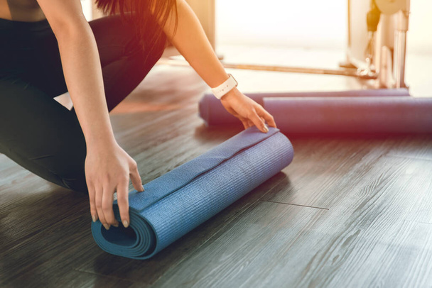Tapis de yoga, femme de forme saine enroulant la feuille de caoutchouc d'exercice pour la classe de démarrage dans le club de sport - Photo, image
