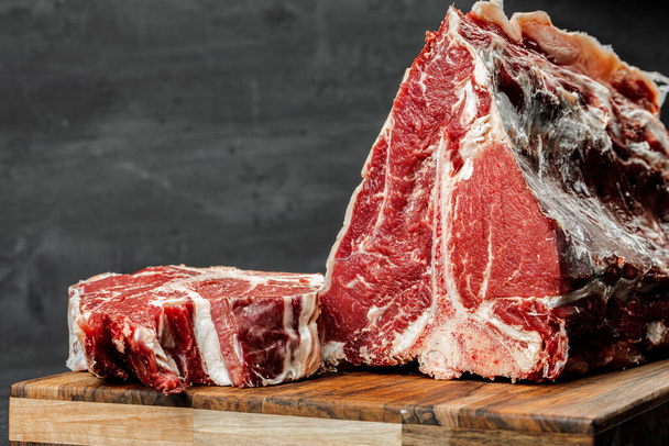 Raw T-bone steak cooking on stone dark table. - Zdjęcie, obraz