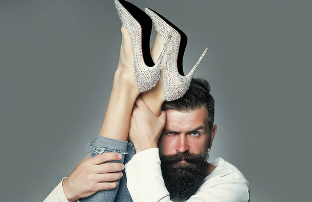 Man holding legs of woman. Portrait of handsome man with beard moustache eyebrow. Diamante high heels. - Zdjęcie, obraz