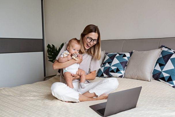 Telecommuting in quarantine. Mother showing baby to friends at the video chat. Stylish young freelancer working from home. Social distancing during coronavirus covid-19 pandemic concept. - Φωτογραφία, εικόνα
