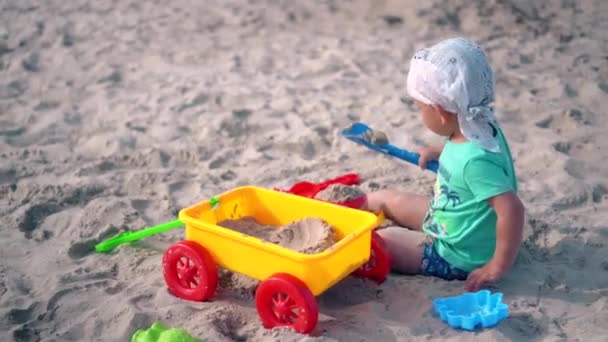 Hermoso niño pequeño jugar con juguetes de colores en la arena de la playa. Movimiento de cámara - Metraje, vídeo
