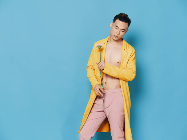 Fashionable man in a yellow coat with a flower in his hand on a blue background, Asian appearance - Foto, imagen