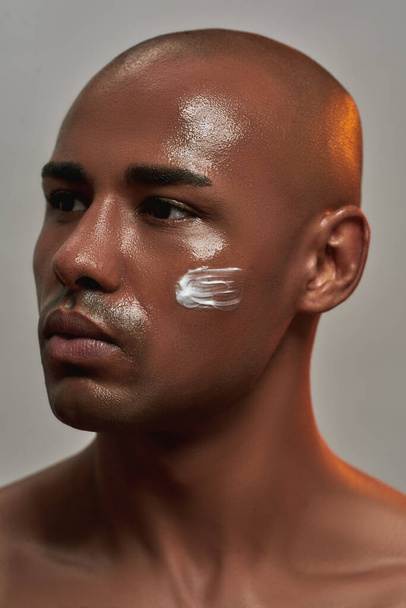 Closeup portrait of handsome young african american man with cream applied on his cheek looking away while posing isolated over gray background - Φωτογραφία, εικόνα