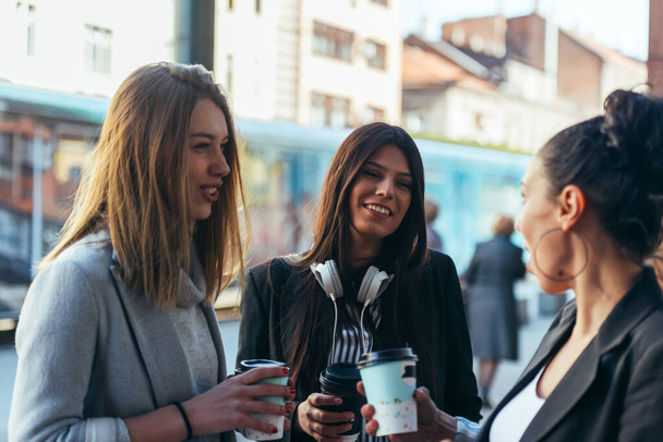 Група дівчат, що стоять на відкритому повітрі і спілкуються один з одним під час пиття кави
. - Фото, зображення