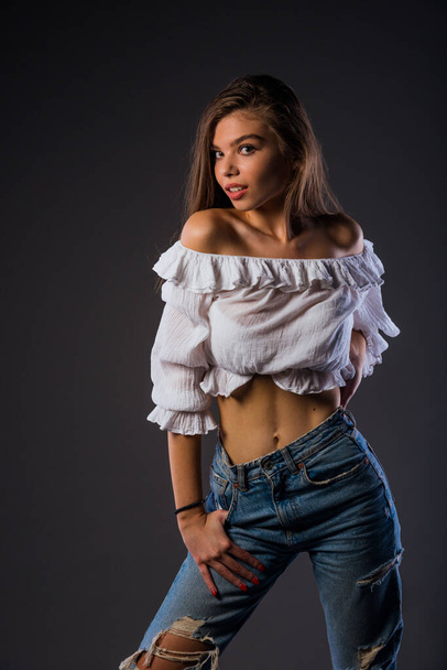 Portrait of a beautiful stylish girl wearing white tank top and blue ripped jeans - Фото, зображення