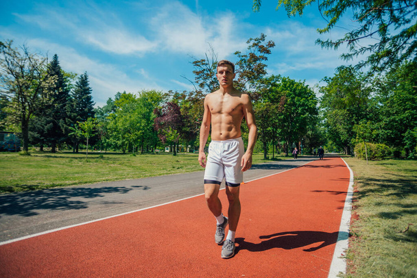 Giovane atleta senza t-shirt cammina su una pista da corsa nel parco - Foto, immagini