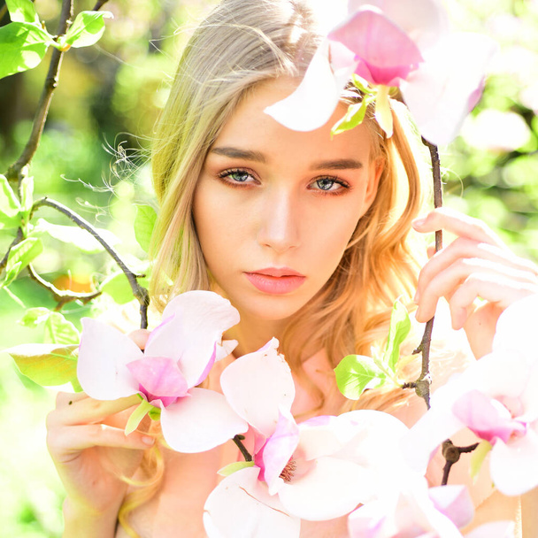 Young woman on dreamy face. Tender blonde teen near magnolia flowers. Young woman enjoy flowers in garden. Spring bloom concept. - 写真・画像