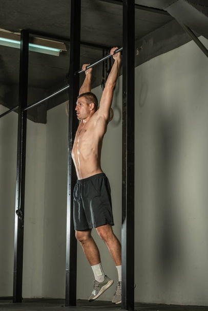 Handsome bodybuilder doing pull-ups on horizontal bar in a indoors modern gym. - Photo, Image