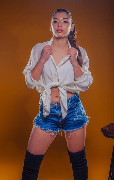 Young woman wearing stylish outfit with a white linen shirt and blue short jeans posing isolated in studio - Photo, Image