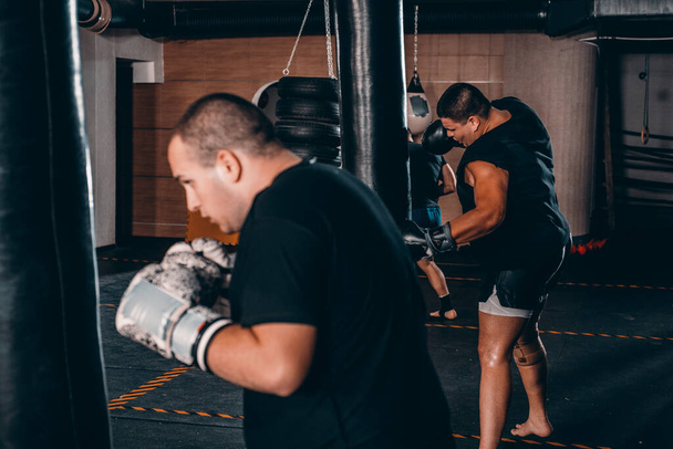 Determinado jovem Muay Thai lutador em luvas de boxe treinamento tailandês de boxe com saco de perfuração
 - Foto, Imagem