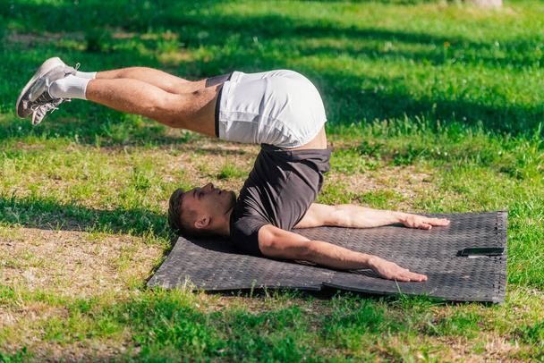 Joven hombre guapo deportivo practicando yoga en el parque y haciendo la pose de arado. - Foto, Imagen