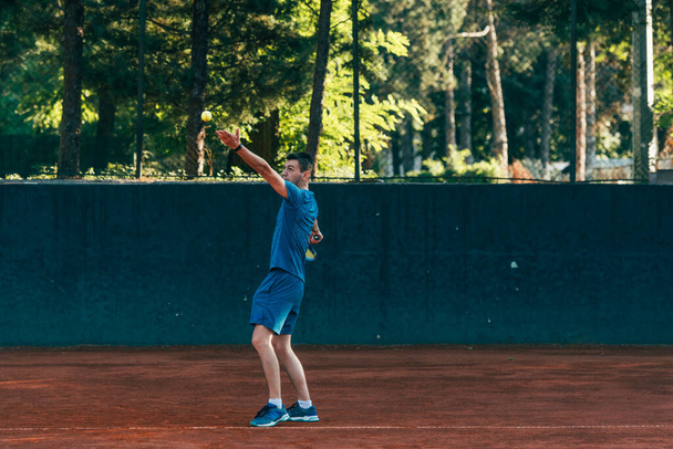 Профессиональный теннисист подает мяч на глиняном теннисном корте - Фото, изображение