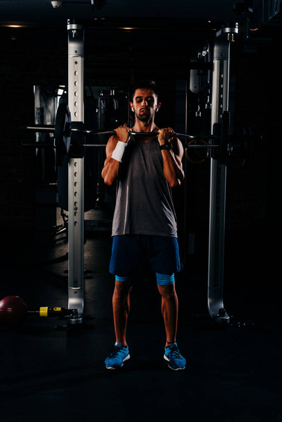 schlanker, muskulöser Mann, der im Fitnessstudio Gewichte stemmt, hoher Kontrast, dunkles Image - Foto, Bild