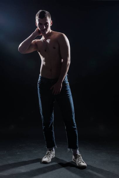 Силуетна картина гарячого без сорочки м'язистого чоловіка позує в джинсах в темній студії
. - Фото, зображення