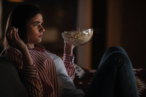 Όμορφη γυναίκα βλέποντας ταινία το βράδυ κάθεται σε έναν καναπέ στο σαλόνι στο σπίτι - Φωτογραφία, εικόνα