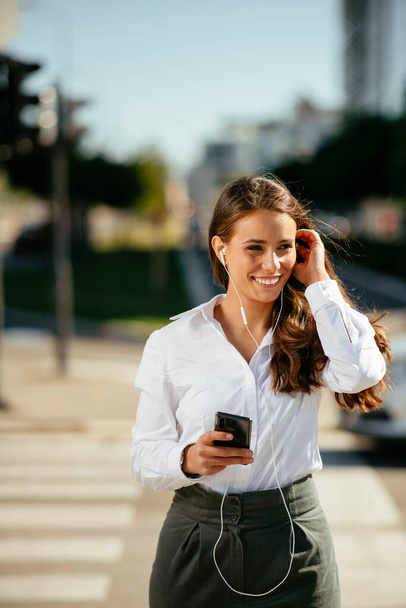 Красива молода бізнес-леді слухає музику з навушниками під час ходьби на вулиці
 - Фото, зображення