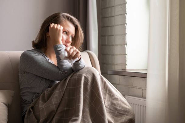 Sick brunette woman with headache having cold and flu sneezing sitting on the couch in the living room near window - Foto, Bild