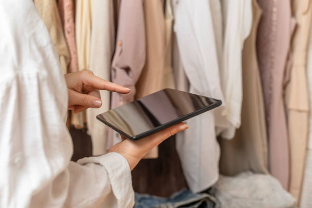 Female entrepreneur holding tablet while doing inventory in her trendy clothing shop - 写真・画像