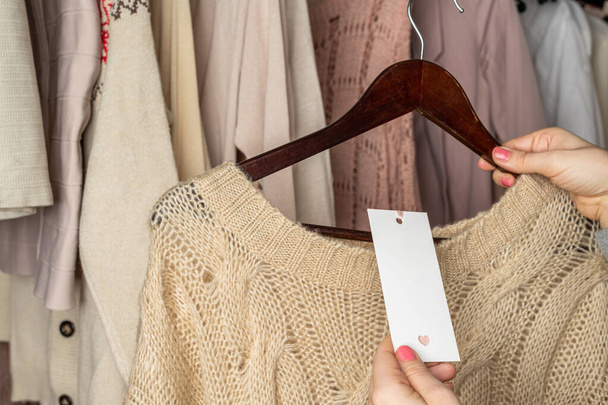 Woman shopper looking on empty tag, template choosing  sweater from clothes in garment store. Shopping. - Foto, Bild