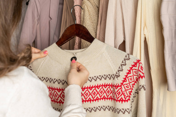 Femme choisissant pull en laine avec ornement de Noël dans le placard de la maison. Concept de saison - Photo, image