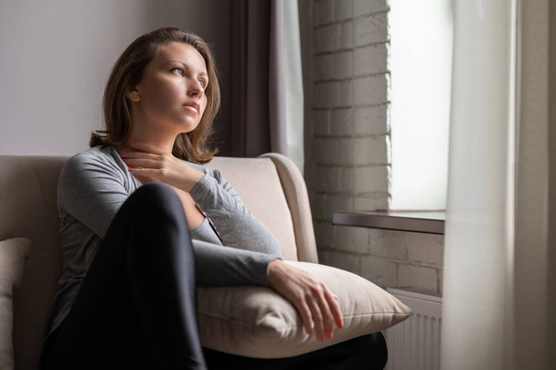 Portrait of lonely sad caucasian young woman sitting near window of apartments. - Foto, Bild