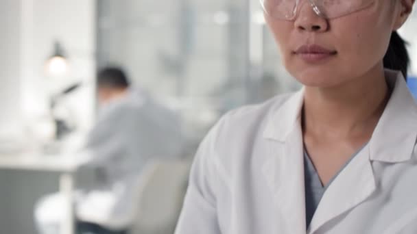 Primer plano de inclinación en cámara lenta de una microbióloga asiática que sostiene una placa de Petri con una muestra de carne cultivada en laboratorio que la examina en laboratorio - Imágenes, Vídeo