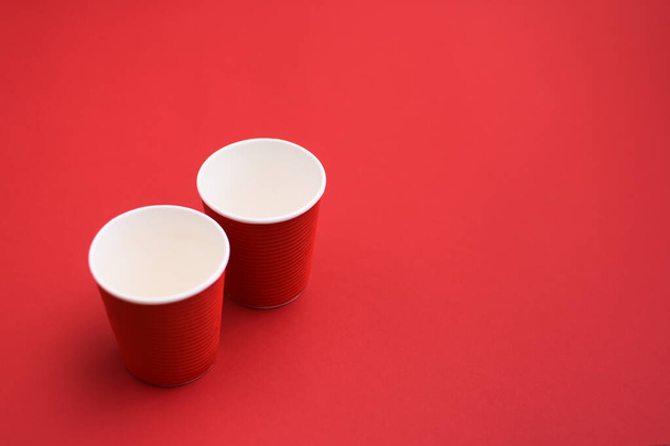 dos vasos de café vacíos de cartón rojo. dos tazas de papel sobre fondo rojo. - Foto, imagen