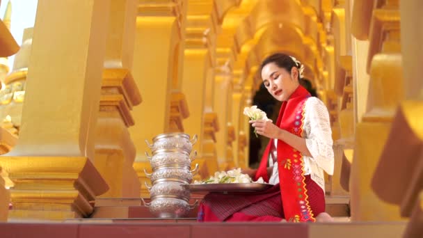 Frauen aus Myanmar mit Blumen an einem Tempel. Südostasiatische junge Mädchen in burmesischer Tracht besuchen einen buddhistischen Tempel. - Filmmaterial, Video