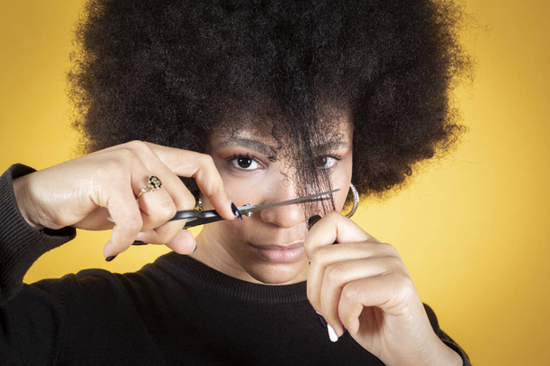 Karışık afro kadın saçını makasla kesiyor, sarı arka plan fotokopi alanı - Fotoğraf, Görsel