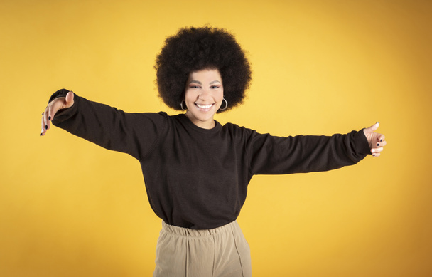 Mixed afro hair woman hugging, smiling, happy, yellow background, copy space - Φωτογραφία, εικόνα