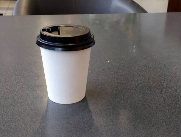 Café en una taza de plástico blanco con una tapa marrón está en una mesa negra. Concepto de comida rápida - Foto, Imagen