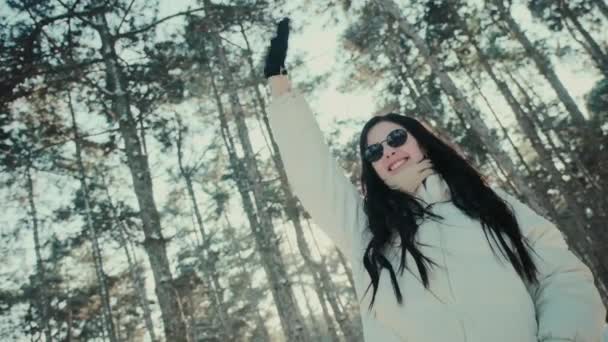 Güneş gözlüklü mutlu kadın kış ormanında el ele sallıyor. - Video, Çekim