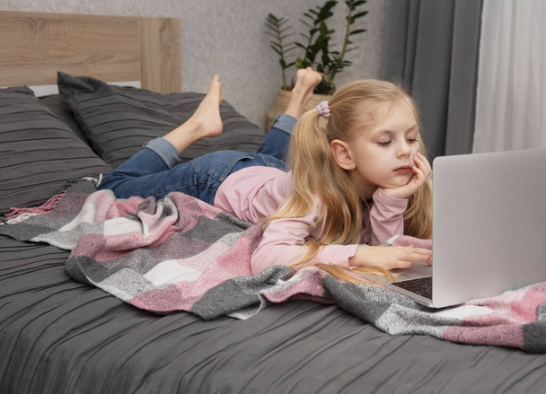 Menina loira estuda em casa online com um laptop na cama - Foto, Imagem