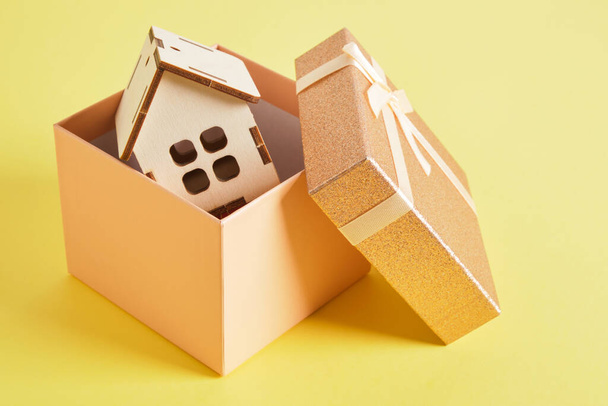 small house model in shiny pink gift box on yellow background - Photo, Image
