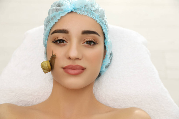 Young woman receiving snail facial massage in spa salon - Foto, afbeelding