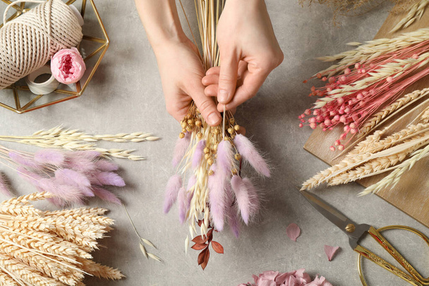 Florist making bouquet of dried flowers at grey stone table, top view - 写真・画像