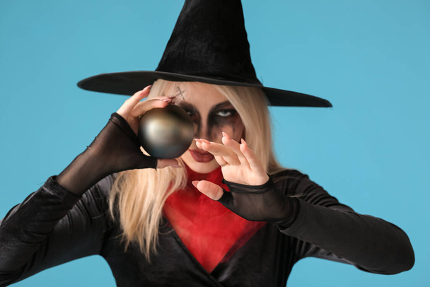 Scary young witch with magic ball on color background - Photo, Image