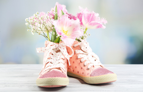 Beautiful gumshoes with flowers inside on wooden table, on bright background - Фото, зображення