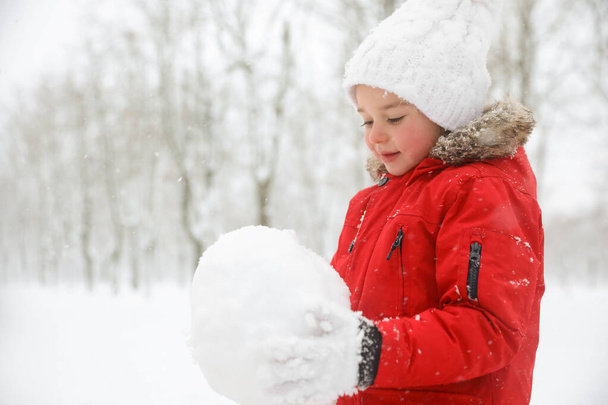 Cute little girl holding snowball outdoors on winter day, space for text - Foto, imagen
