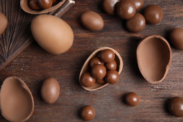 Tasty chocolate eggs and candies on wooden table, flat lay - Fotografie, Obrázek